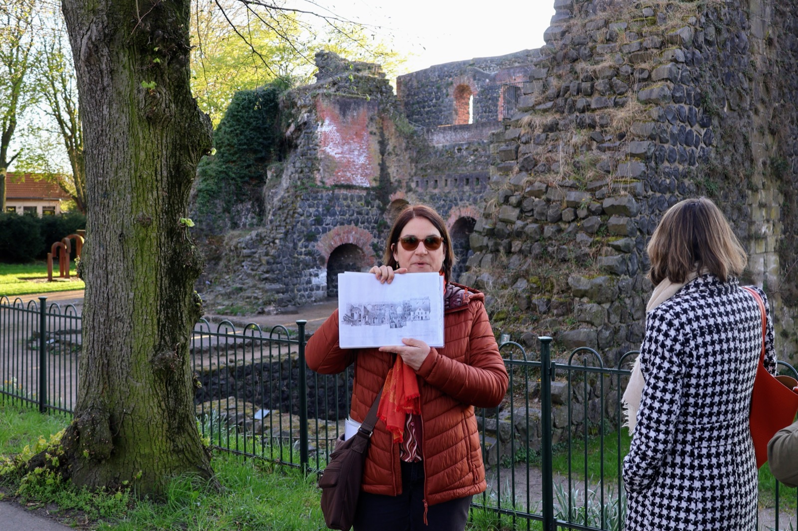 Dr. Büttner zeigt eine historische Abbildung vor der Ruine der Kaiserpfalz