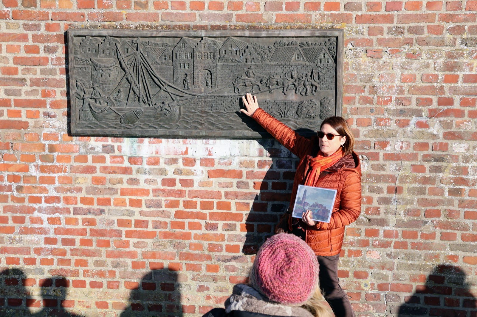 Dr. Büttner erklärt ein historisches Stadtrelief an einer Backsteinmauer